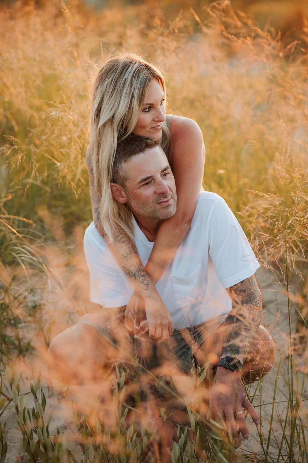 Romantic couple embracing in tall golden grass during a warm sunset photo session.