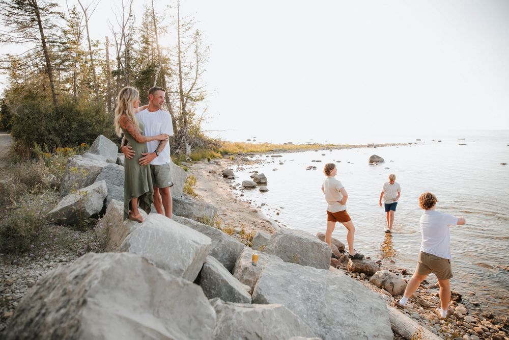 Family enjoying a sunny day on Lake Michigan shoreline, with couples embracing and children wading in calm lake water.