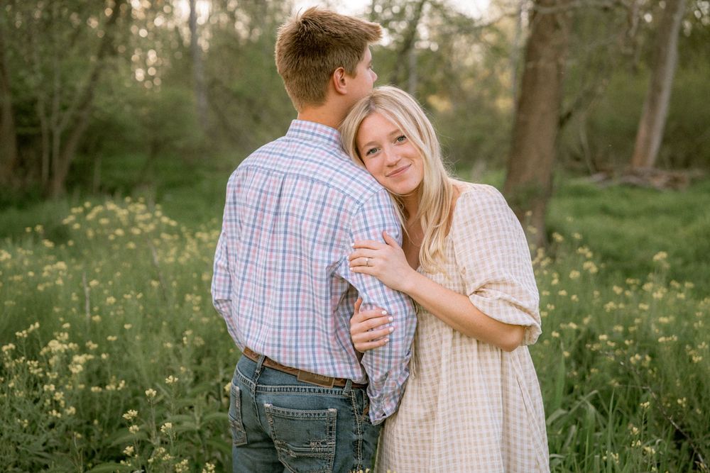 Couple embracing in a wildflower meadow, woman in beige dress smiling over mans shoulder during golden hour.