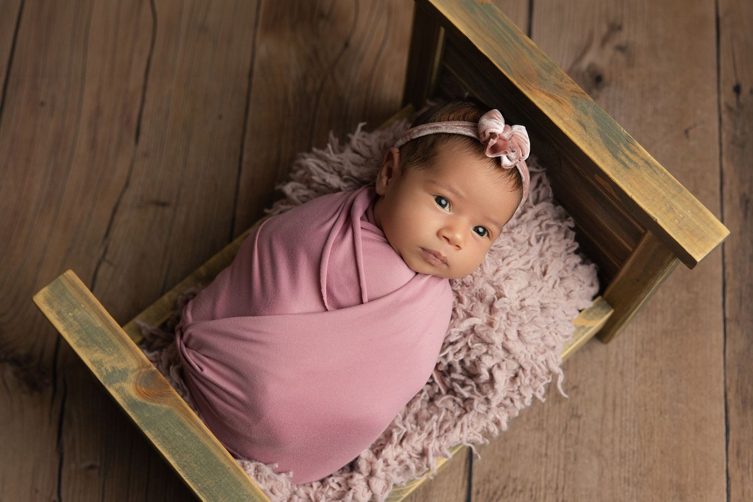 Newborn baby resting chin on hands inside a teal bucket with soft blanket, studio photography.