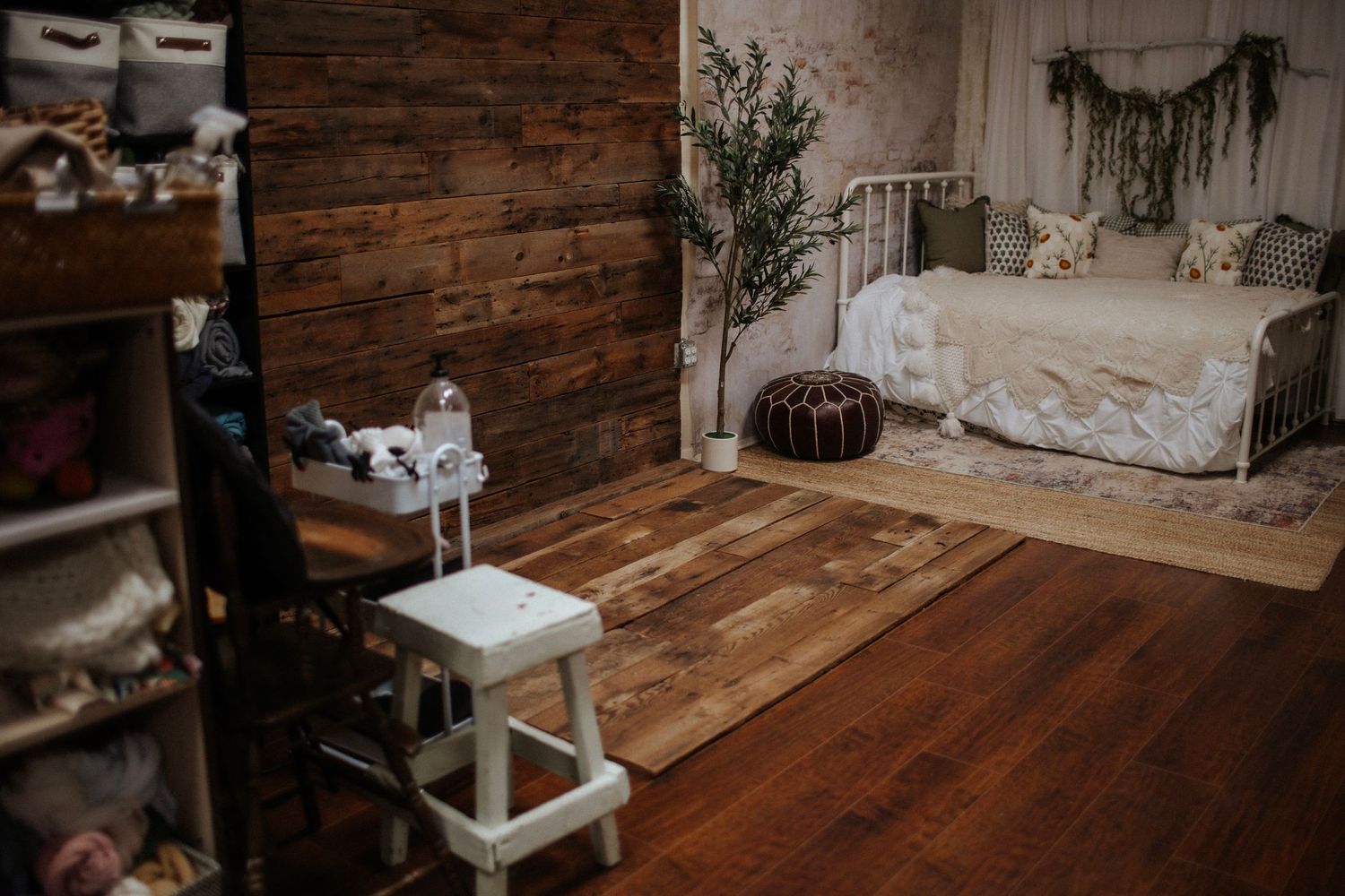 Rustic children's room with wood plank walls, hardwood floors, white stool, iron daybed, and boho decor.