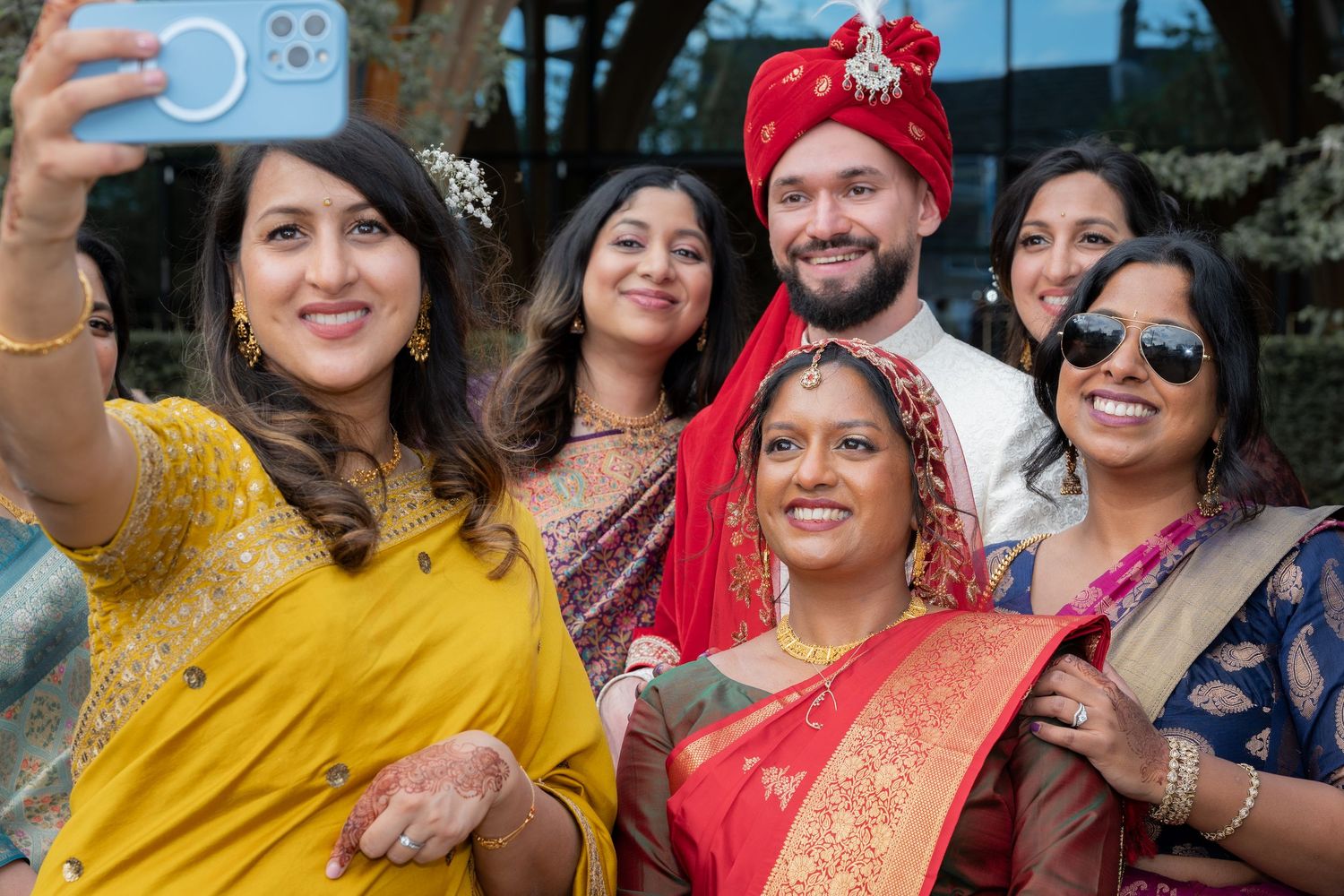 Group of people in traditional Indian attire taking a selfie at a wedding celebration.