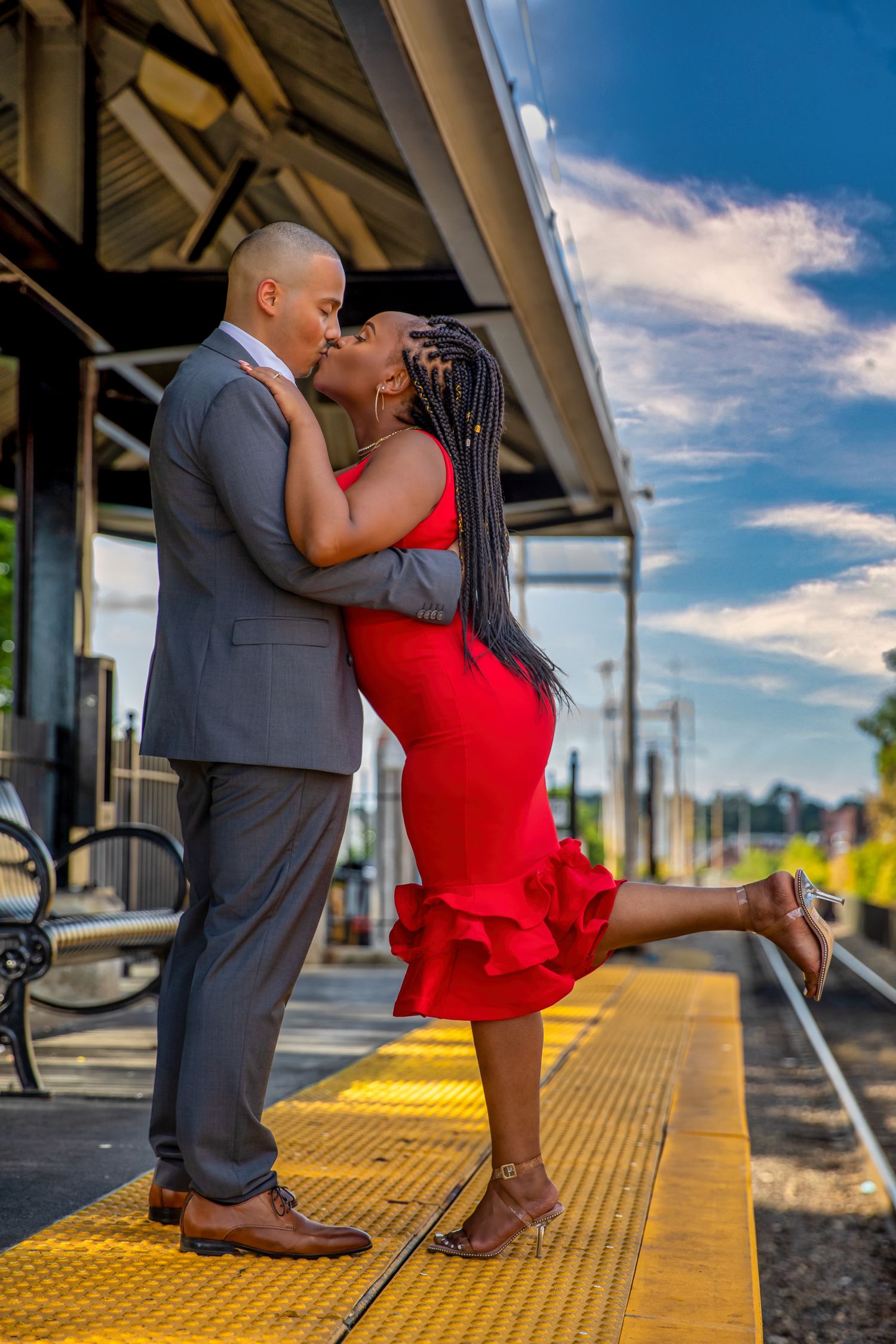 Romantic couple in formal attire sharing intimate moments at a train station platform.
