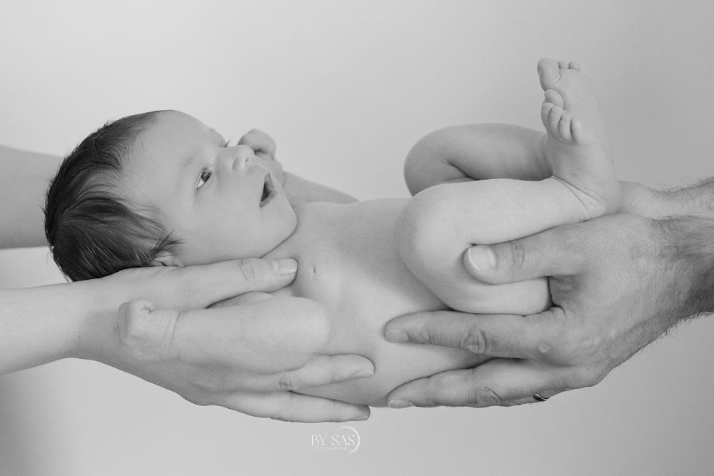 Black and white photo of a newborn baby cradled gently in the hands of two parents.