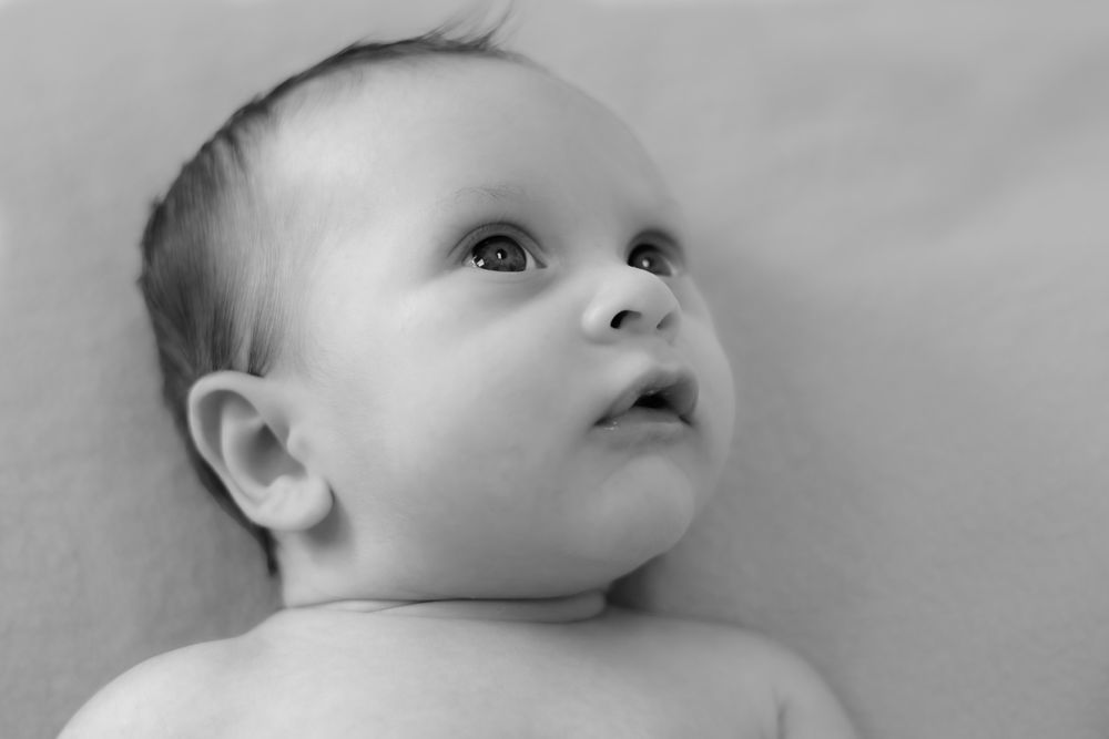 Black and white portrait of a curious newborn baby looking up with wide eyes.