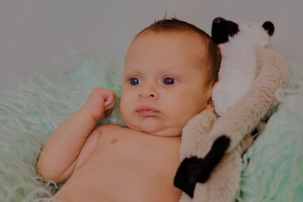 A newborn baby with blue eyes lying on a soft green blanket next to a black and white panda stuffed animal.
