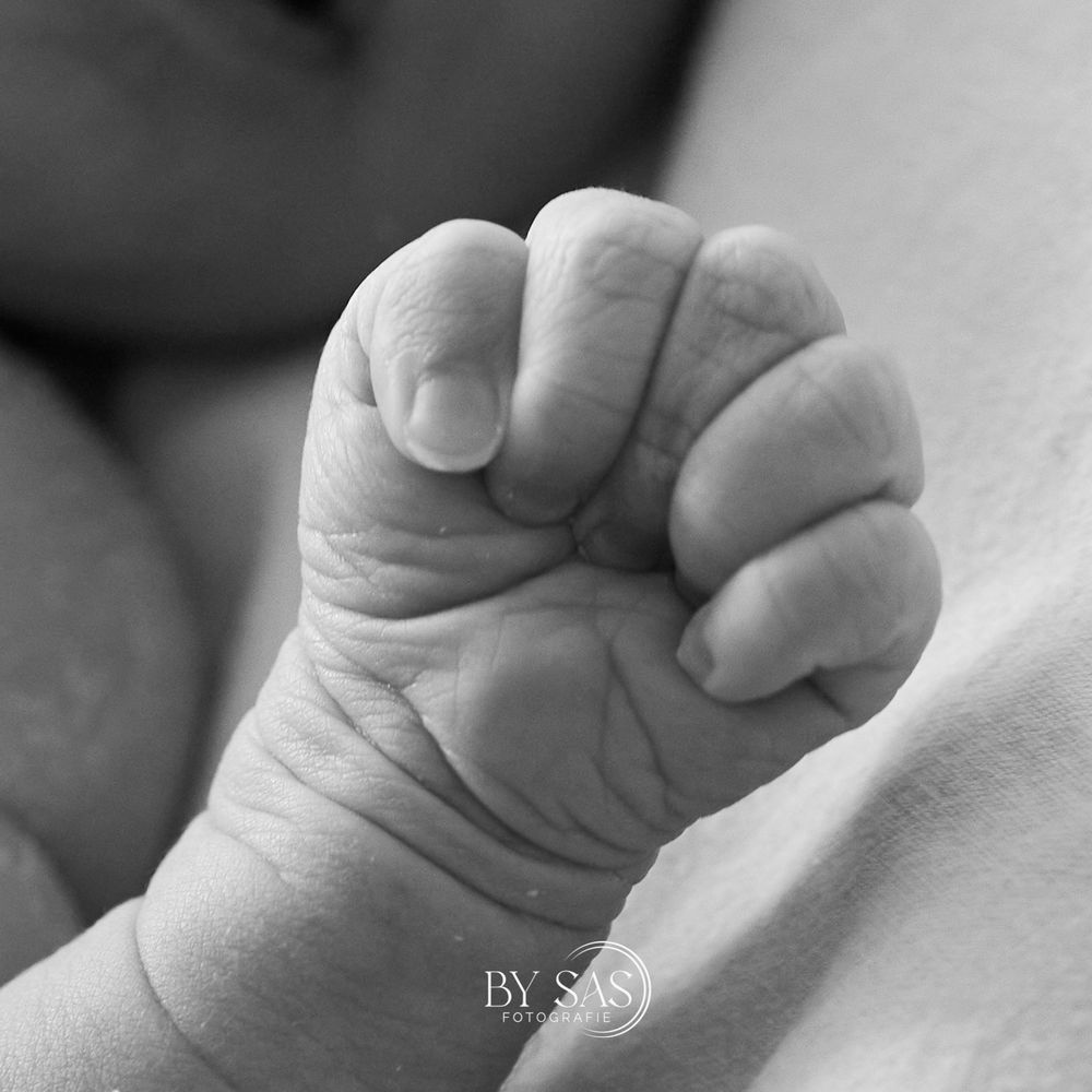 Black and white close-up photo of a newborn baby's tiny clenched fist, capturing delicate skin details.