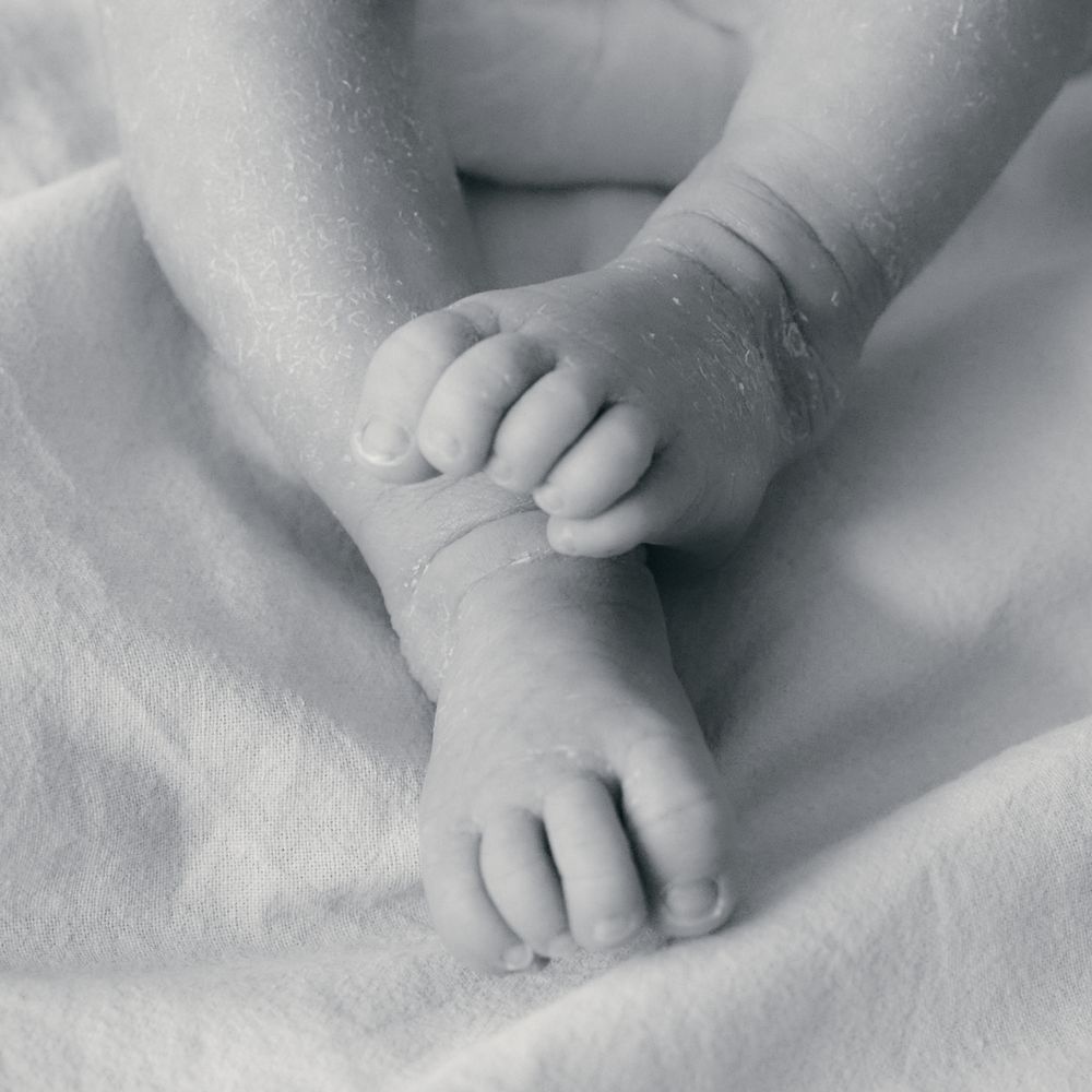 Close-up black and white photo of a newborn baby's tiny hands and feet resting on a soft white blanket.
