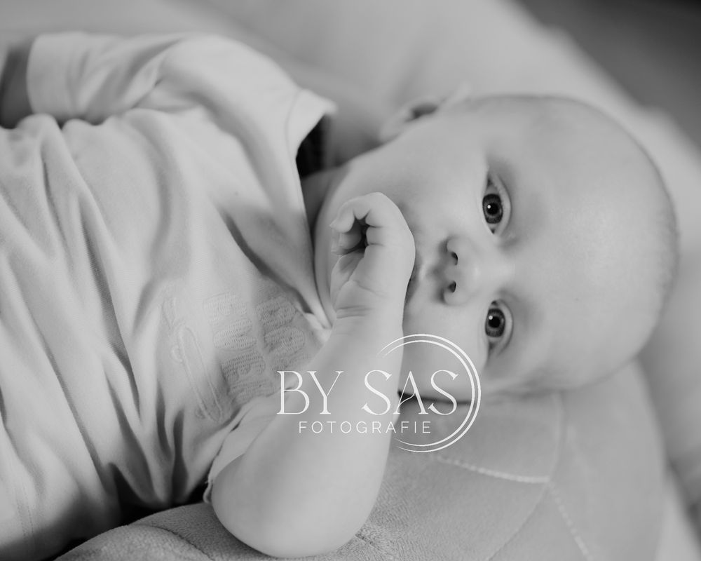 Black and white photo of a newborn baby lying down, gently touching their face with tiny fingers.