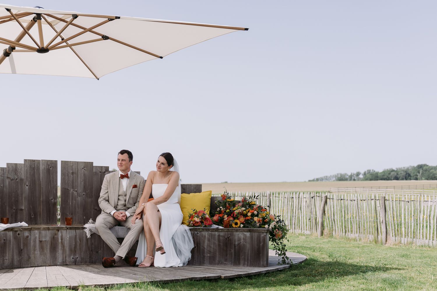 Bride and groom sitting together on a wooden deck under a patio umbrella at a vineyard wedding venue.