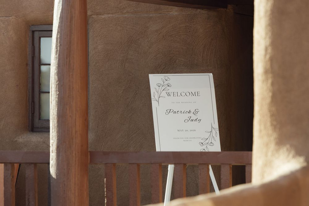 Welcome sign on easel for Patrick and Judy's wedding, displayed outdoors near rustic adobe building.