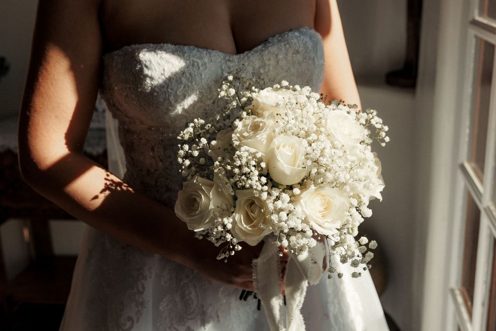 Bride holding a white rose and baby's breath wedding bouquet in a strapless lace gown.