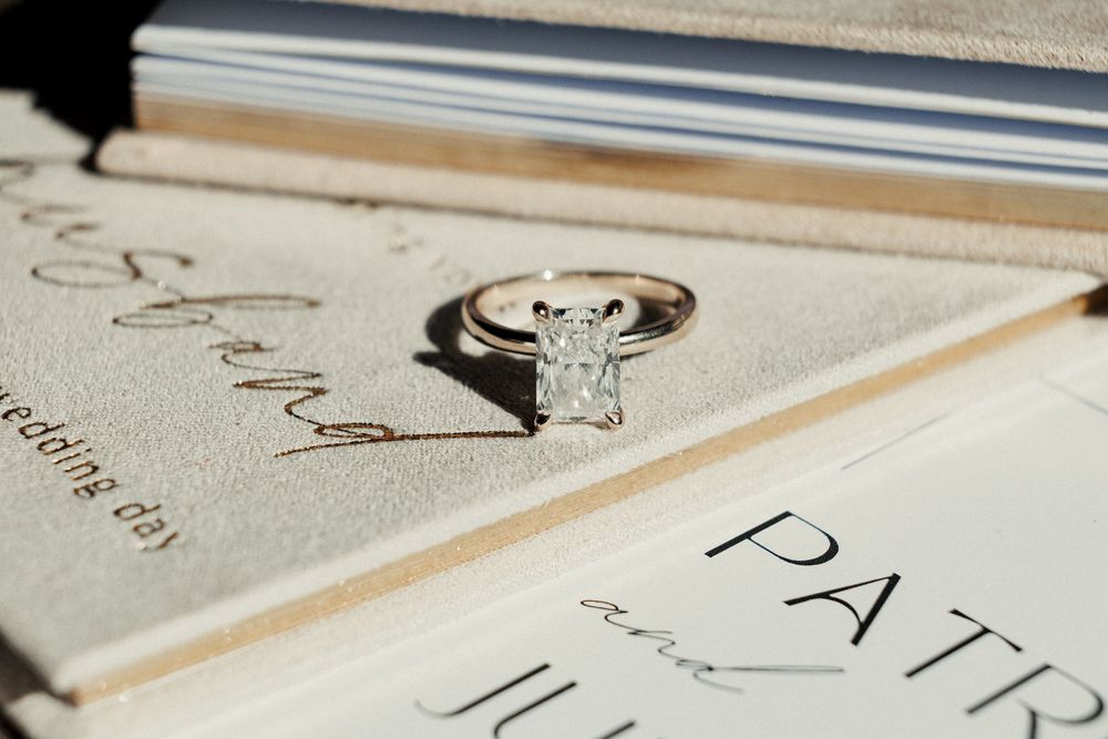 A sparkling diamond solitaire engagement ring resting on elegant wedding stationery in soft natural light.