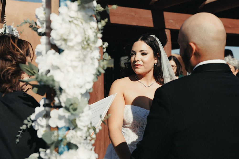 Bride and groom exchanging vows at outdoor wedding ceremony with white floral arch.