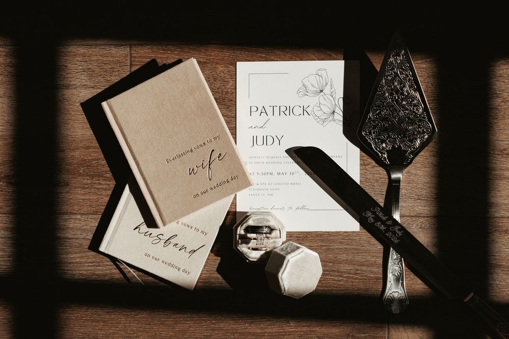 Wedding stationery flat lay featuring Patrick and Judy invitation, vow books, rings, and elegant calligraphy pen on wood.