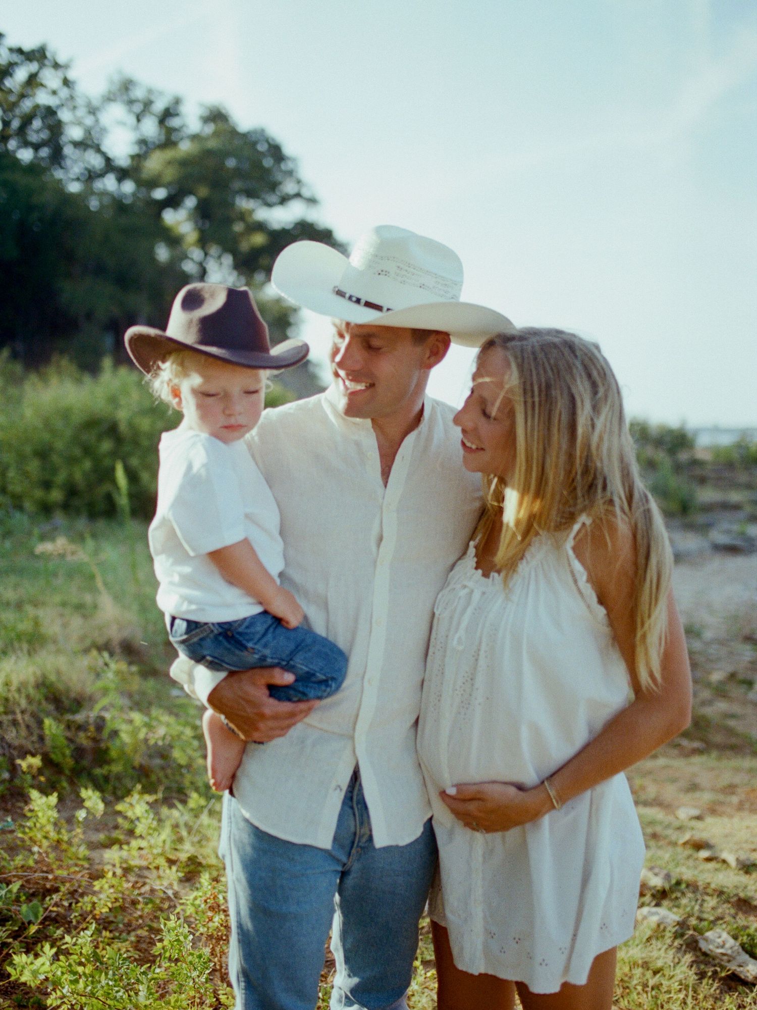 Father in a cowboy hat holding his toddler son beside mom in a Texas field