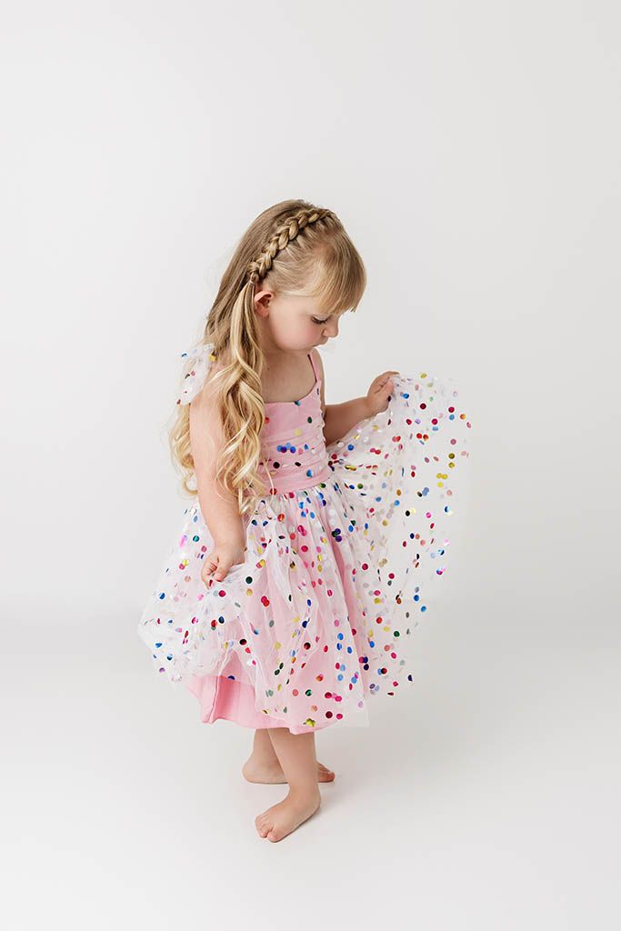 Young girl in pink confetti tulle dress twirling barefoot against white background by Murrieta child photographer..