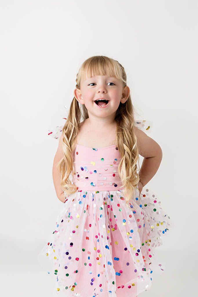 Excited young girl in a pink polka dot tulle dress with hands on hips against white background.
