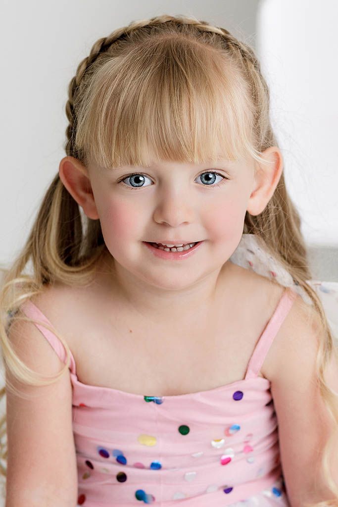 Smiling young girl with blonde pigtails and blue eyes wearing a pink confetti dot dress by Murrieta child photographer.