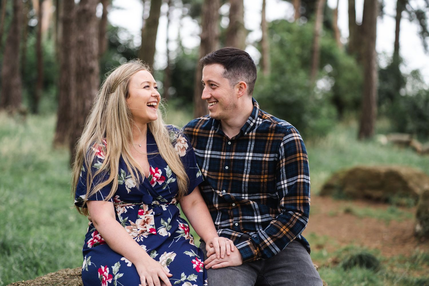 Happy couple laughing together while sitting outdoors in a lush green forest setting.