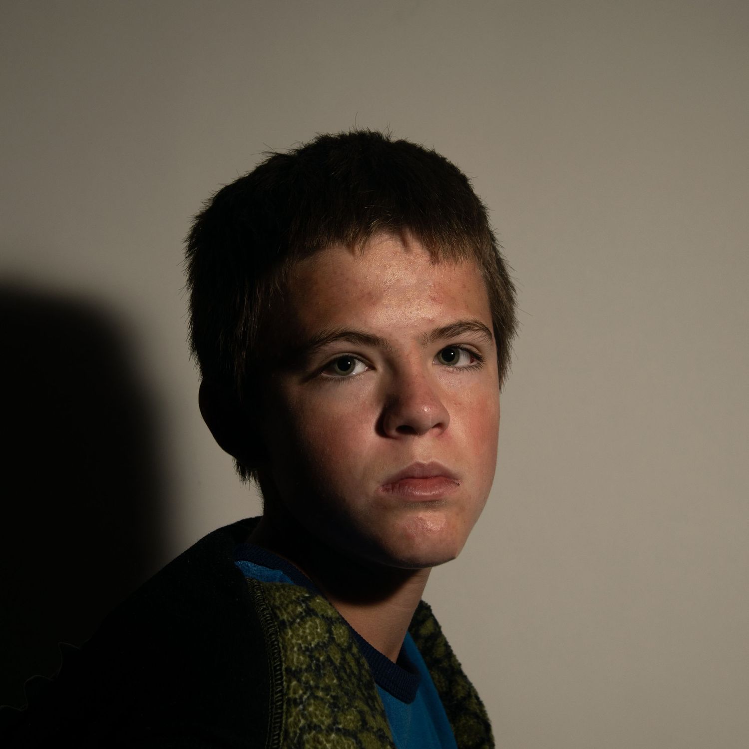 A young boy with short brown hair gazes upward in dramatic side lighting against a neutral background.