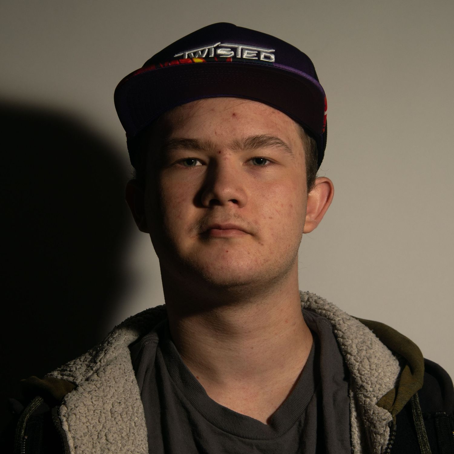 Young man wearing a Twisted snapback cap and hoodie posing against a dark background.