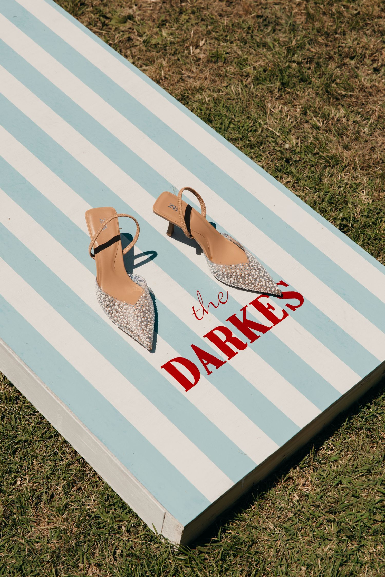 Sparkling bridal heels displayed on a blue and white striped board reading The Darkes on green grass.