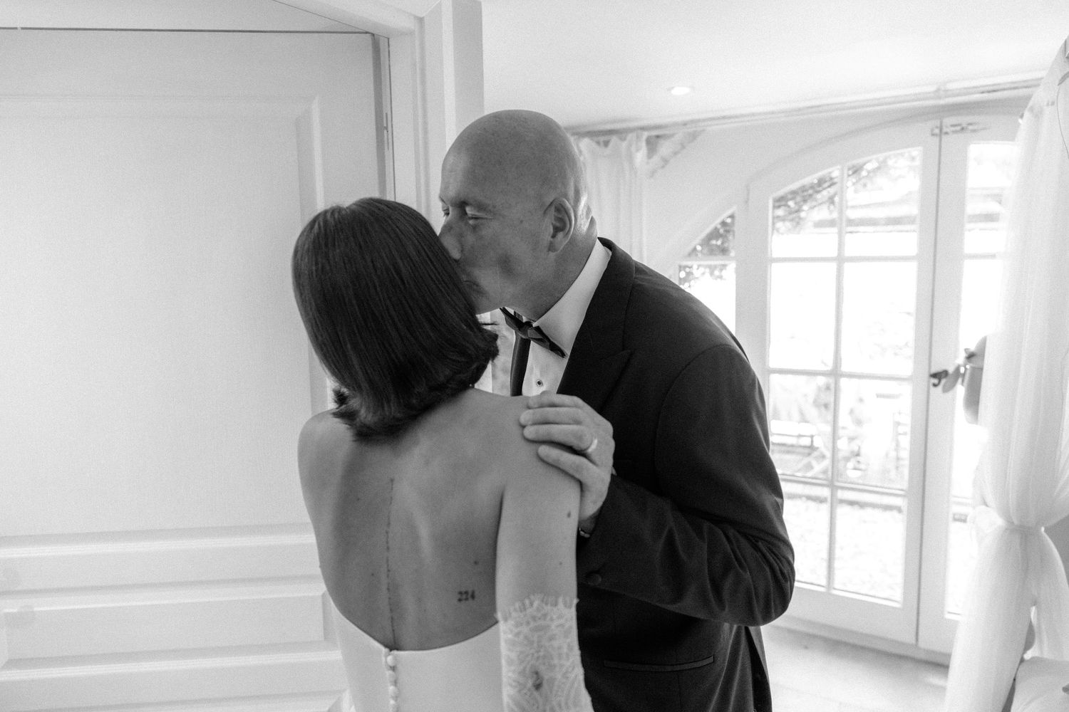 Emotional black and white photo of bride receiving a kiss from her father before the wedding.