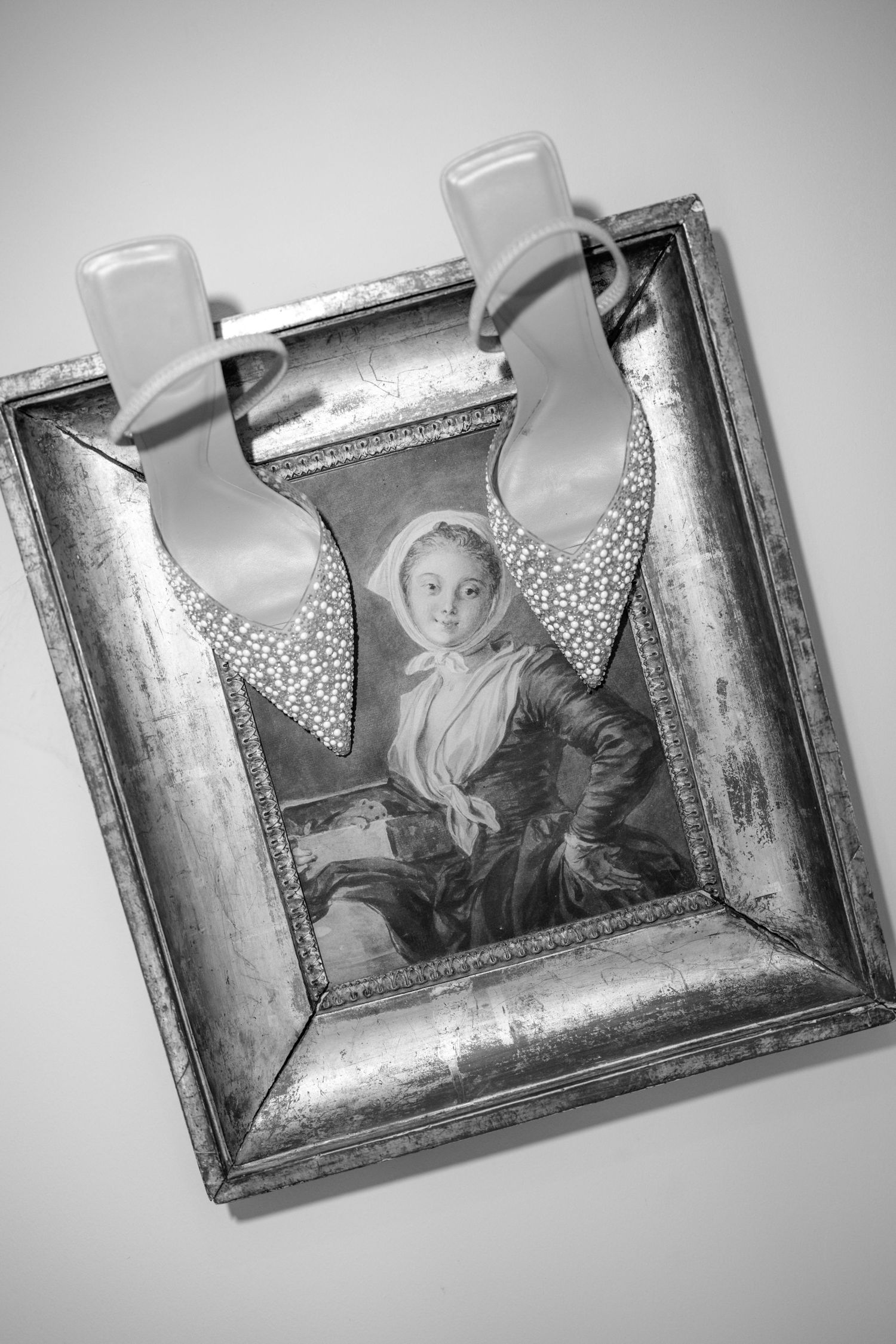 Vintage silver framed portrait of a young woman hanging with decorative ribbon clips on wall.