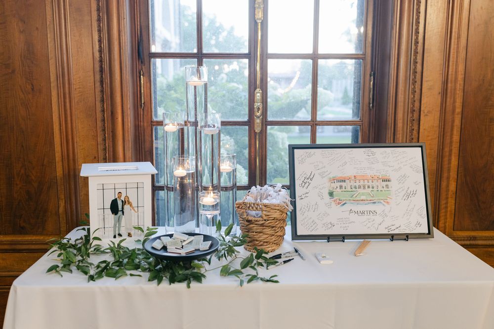 Elegant wedding reception table with candles, greenery garland, cake topper figurines, and a custom illustrated guest book sign.