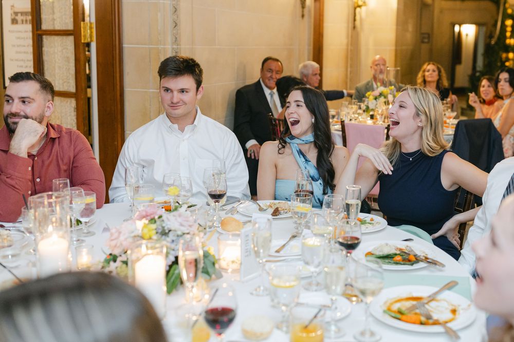 Guests laughing and enjoying dinner at an elegant wedding reception with candlelit tables and formal place settings.