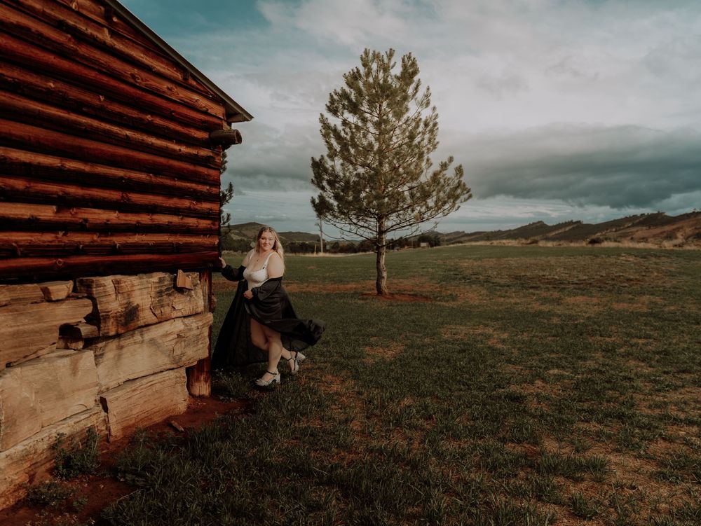 Woman poses with wood building for dramatic, cinematic, portrait, and modeling photos in Fort Collins, Colorado