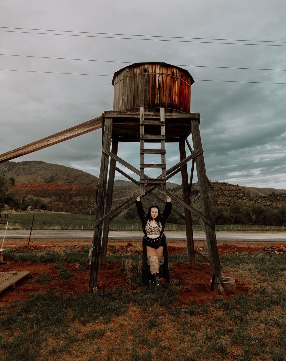 Woman poses and leans on water tower for dramatic, cinematic, portrait, and modeling photos in Fort Collins, Colorado