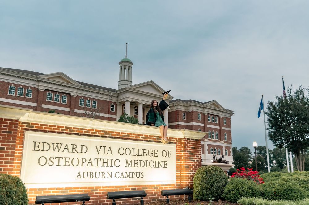 Graduate posing at Edward Via College of Osteopathic Medicine Auburn Campus sign.