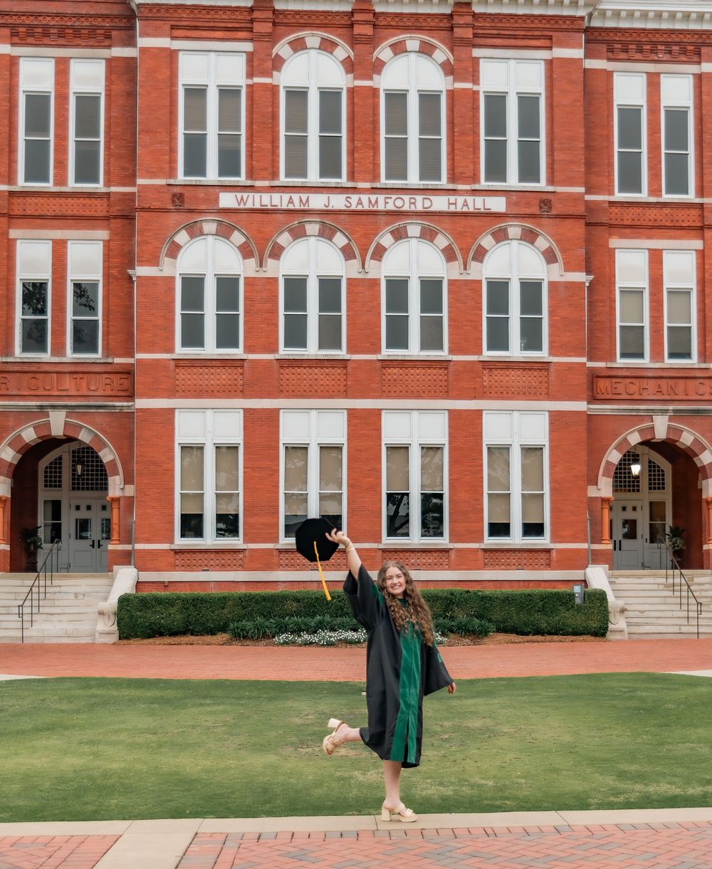 Auburn University graduate in cap and gown celebrating in front of William J. Samford Hall.