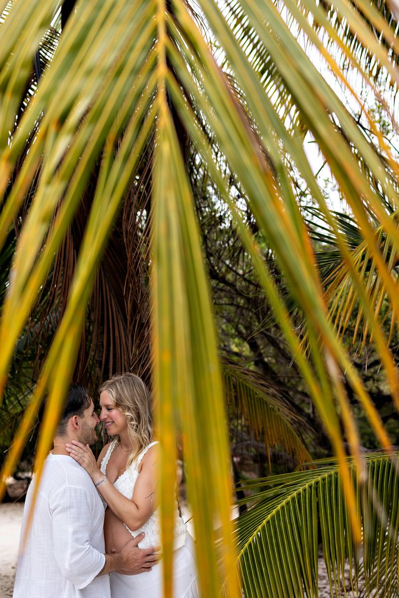 Romantic couple embracing under lush tropical palm fronds in an outdoor setting.