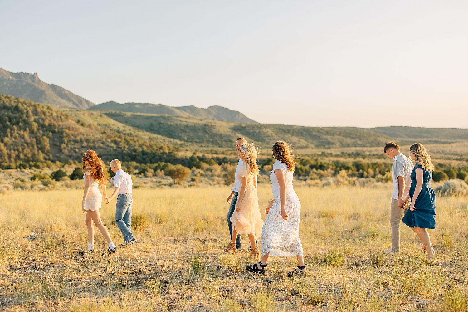 Group of people walking through golden meadow with mountain backdrop during golden hour sunset.
