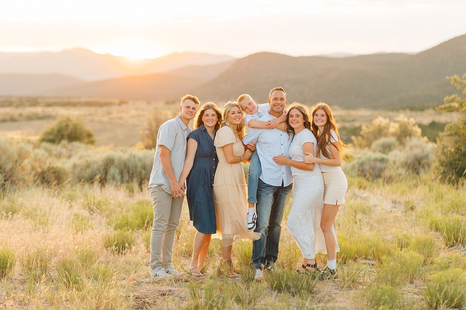 Family of seven posing together at golden hour in a scenic desert landscape with mountains in the background.