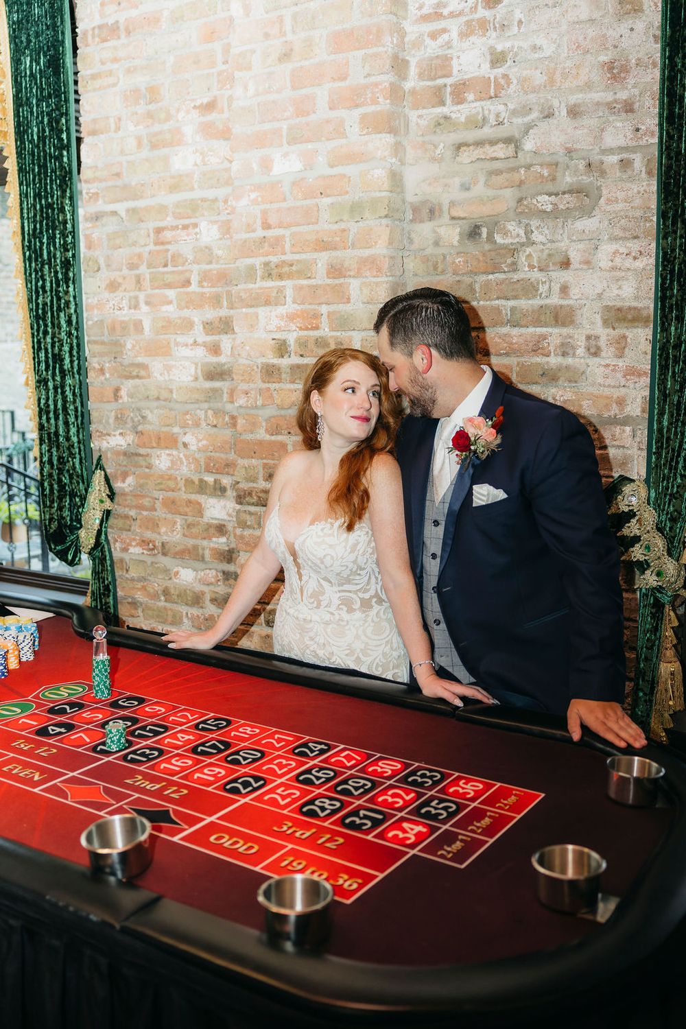 Bride and groom share a romantic moment at a roulette table, with exposed brick walls in an elegant casino-themed wedding in Saint Charles