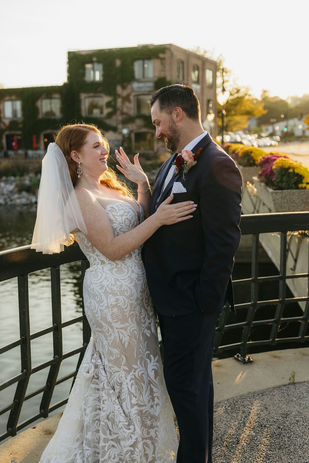 Bride and groom laugh together on waterfront bridge at golden hour during outdoor wedding portraits in Saint Charles, IL
