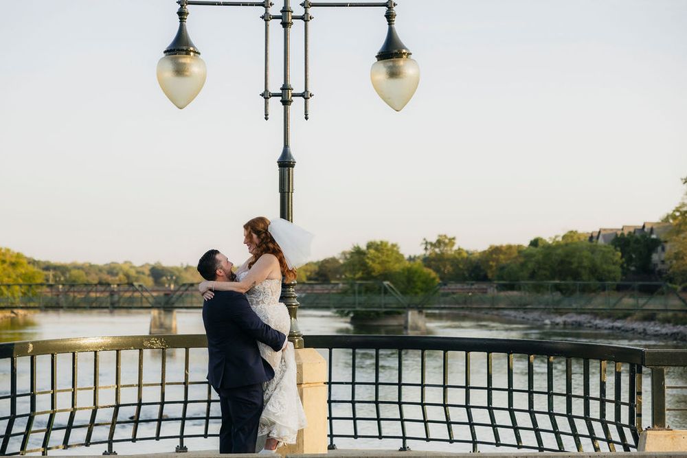 Bride and groom embracing on a bridge with Fox river and trees in the background at sunset in Saint Charles, IL