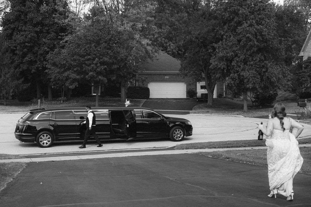 Black and white photo of a bride approaching a stretch limousine with a chauffeur standing by the open door in Saint Charles, IL