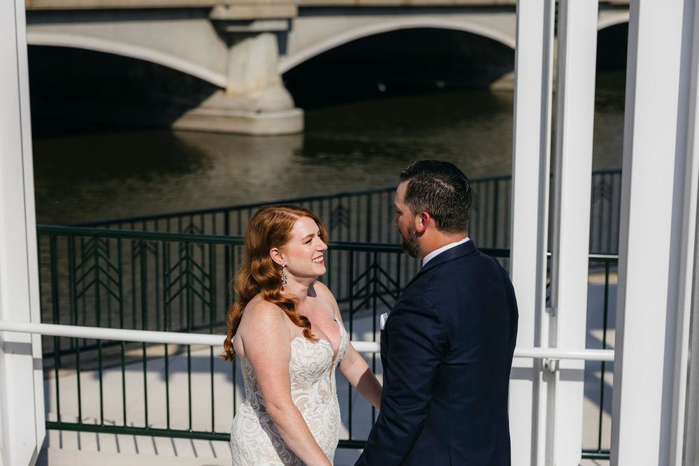 Bride and groom share a romantic moment on a waterfront balcony, with a bridge and Fox river visible in the background in Saint Charles, IL
