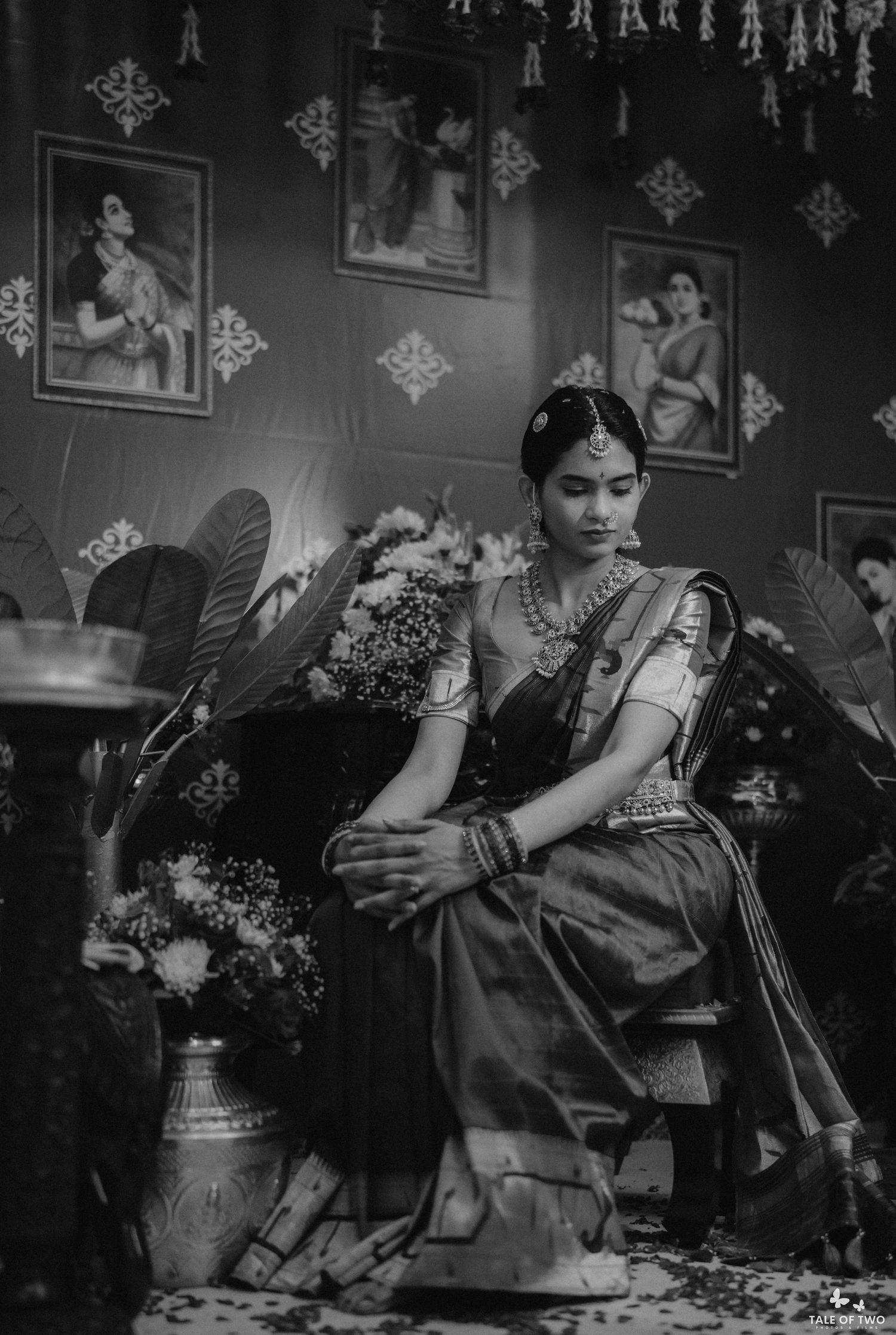 Black and white portrait of South Indian bride in silk saree with gold jewelry seated elegantly at traditional ceremony.