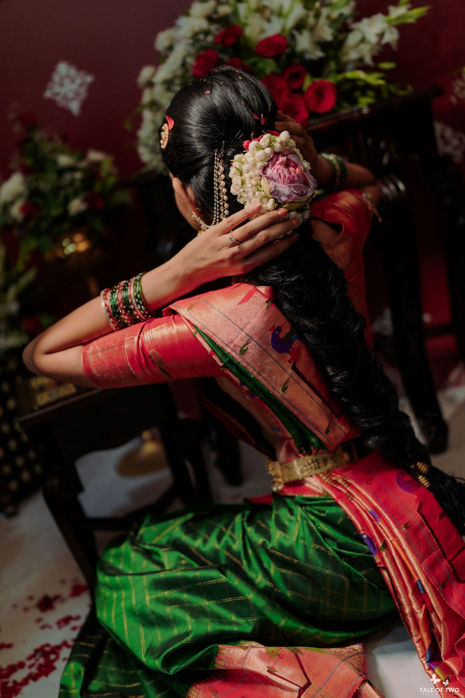 A South Indian bride in a green and pink silk saree adorning her hair bun with fresh flowers at her wedding ceremony.