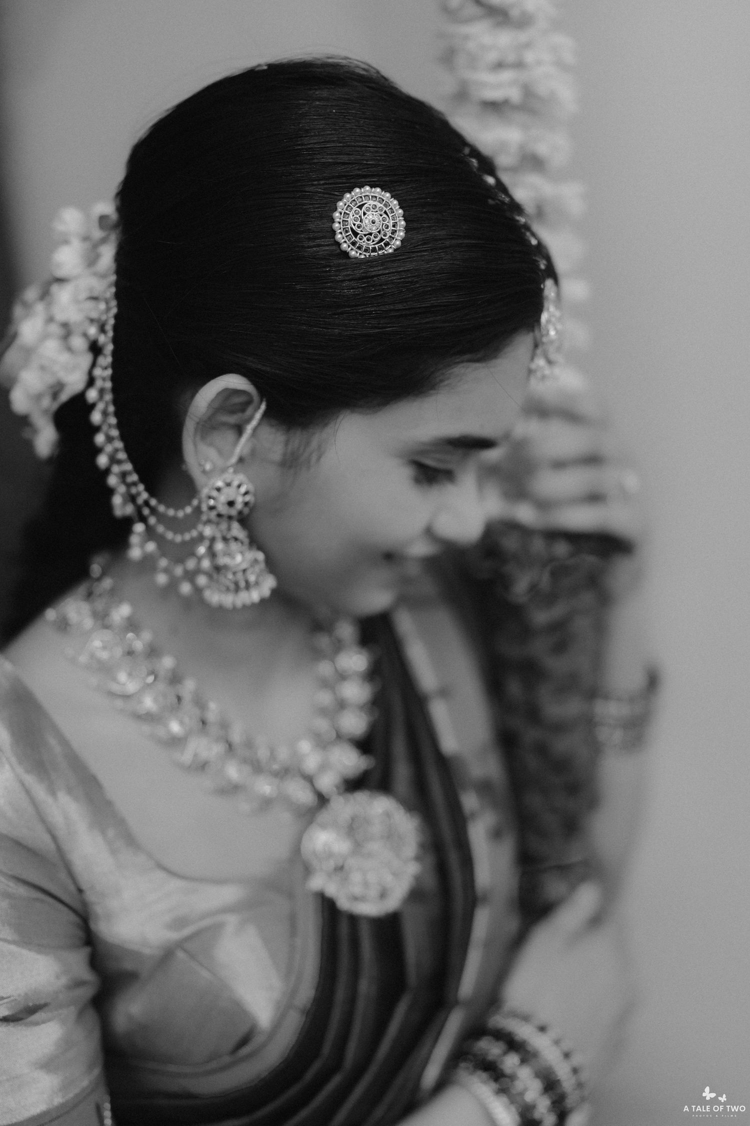 Black and white portrait of Indian bride in silk saree with pearl necklace and floral hair accessories.