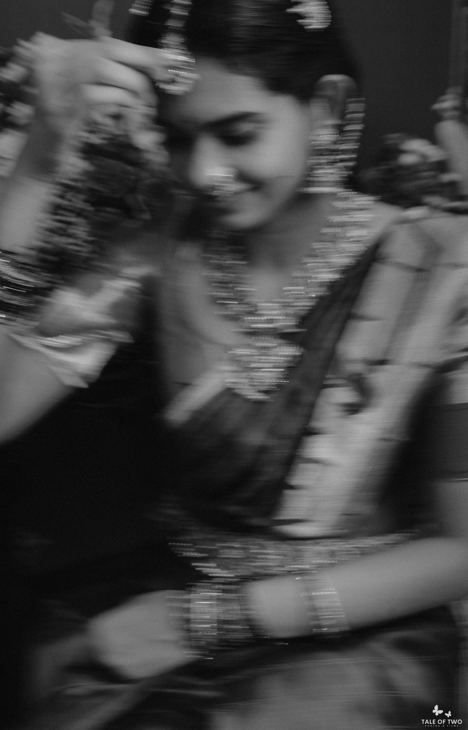 Black and white photo of a South Indian bride smiling while adjusting her hair jewelry during bridal preparation.