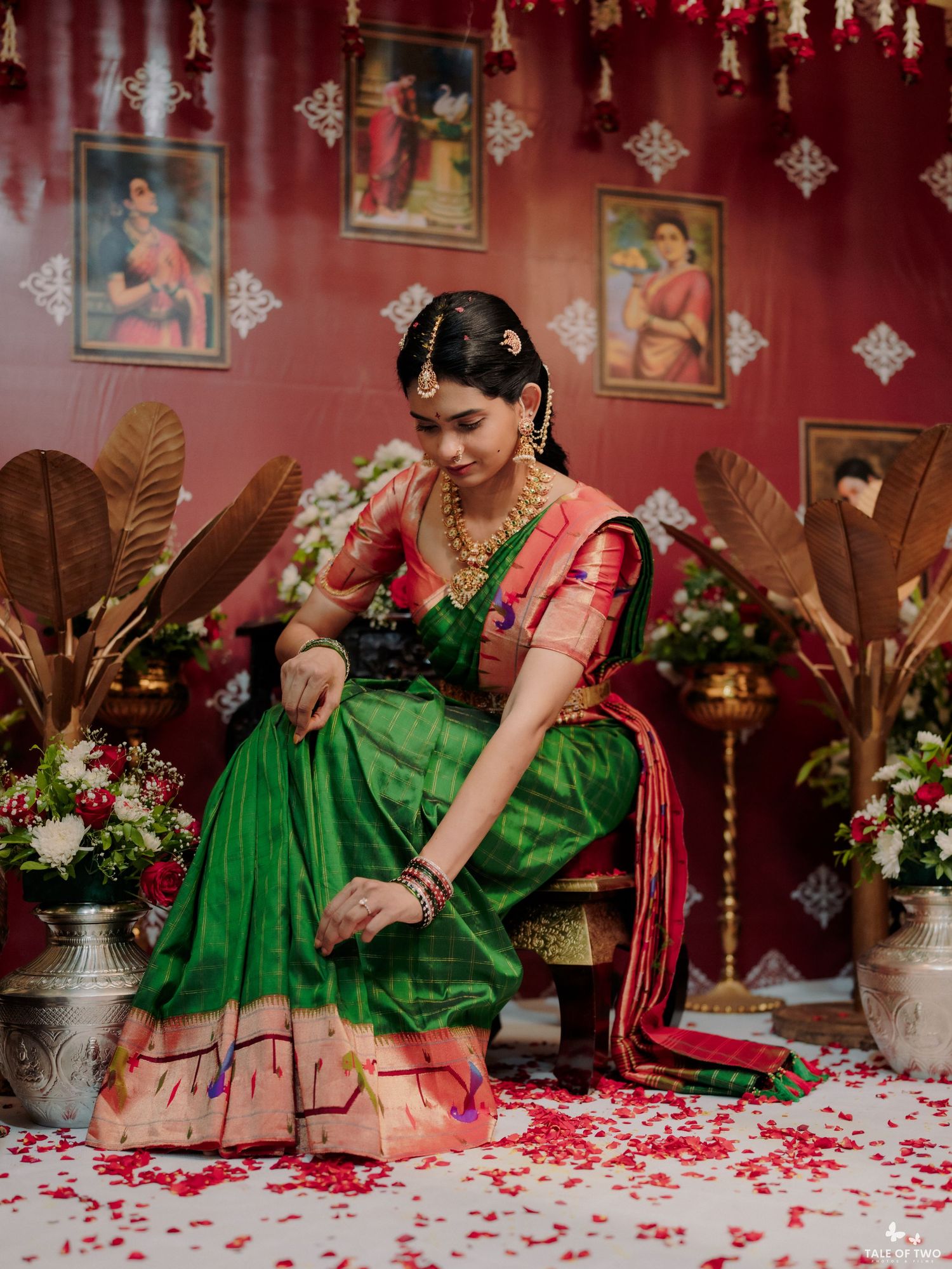 Indian bride in green and pink Kanjivaram silk saree with gold jewelry seated among rose petals.
