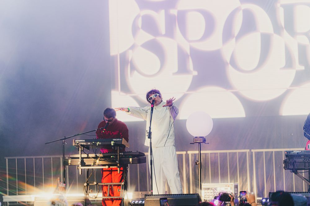 Live concert performer in white outfit on stage with keyboard player and illuminated SPOD logo backdrop.