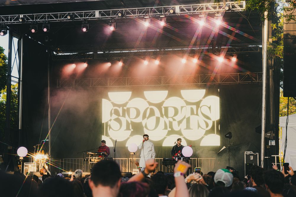 Sports band plays live on a illuminated outdoor stage with fans cheering at a vibrant music festival.
